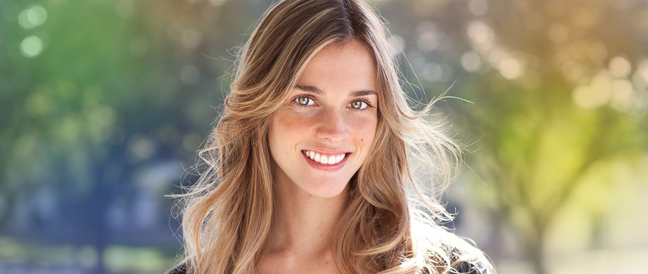 Young blonde woman smiling against a sunlit background