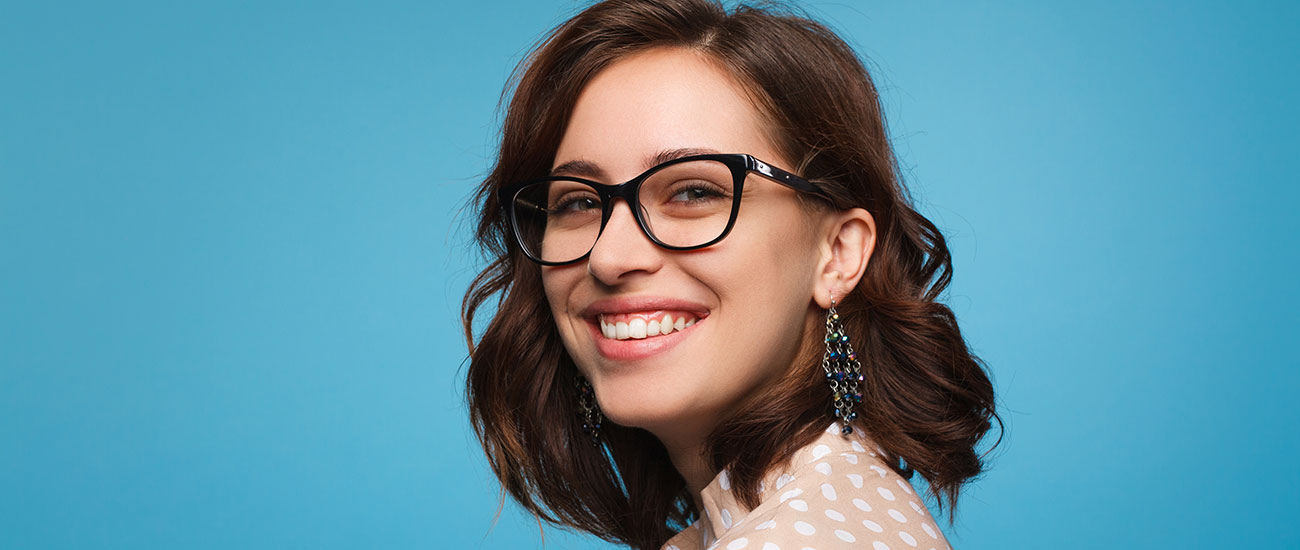 Woman with dark hair and glasses against a blue background, smiling.