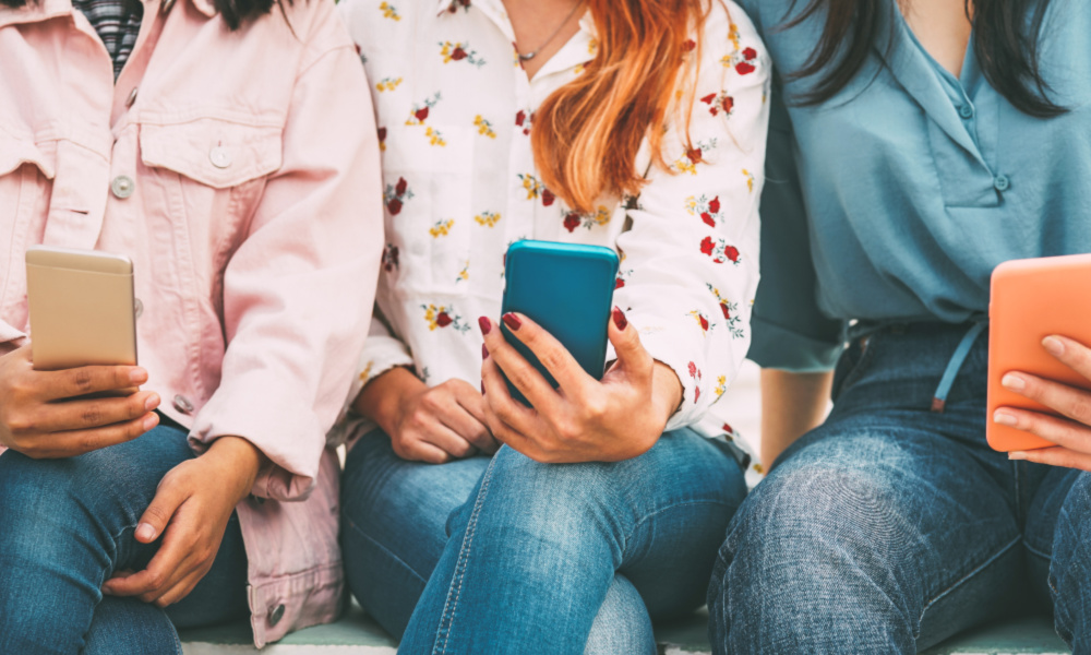 Young women sitting side by side holding smartphones.