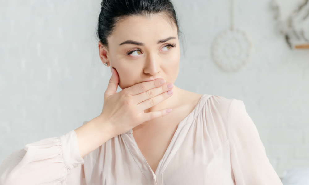 Woman holding hand over her mouth, experiencing nausea.