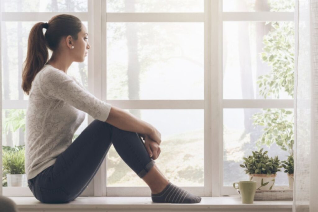 Young woman sitting in windowsill looking outside