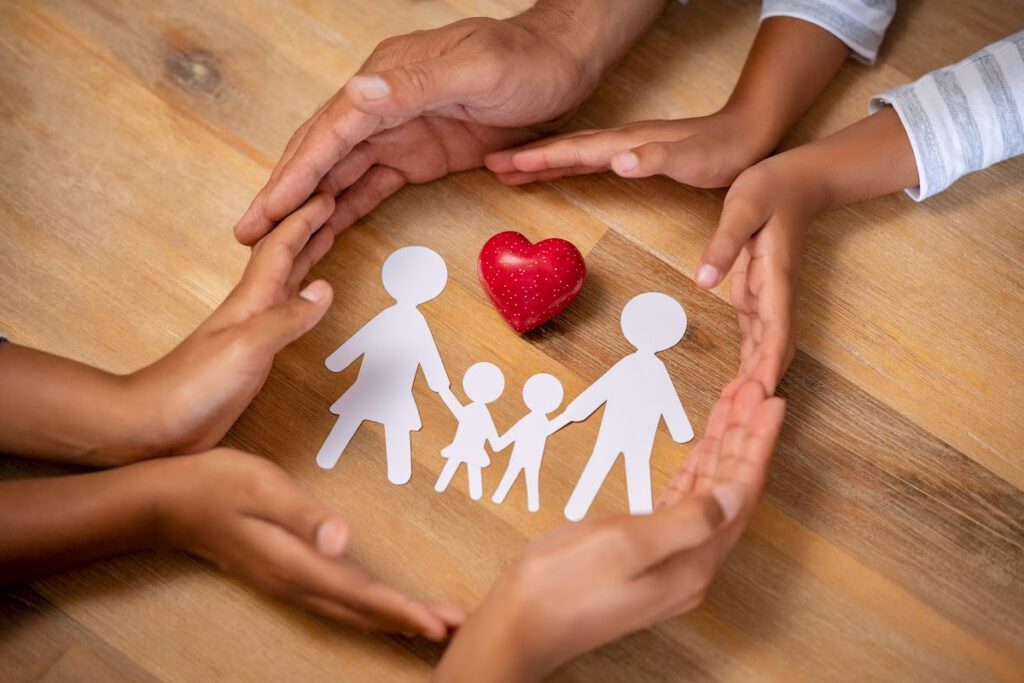 Paper doll cutout of a family surrounded by hands and a red heart.