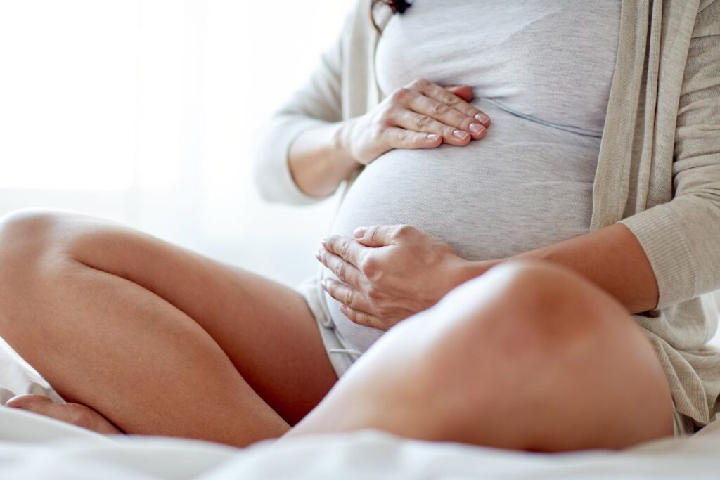 Woman sitting cross-legged with her hands cradling her pregnant belly.