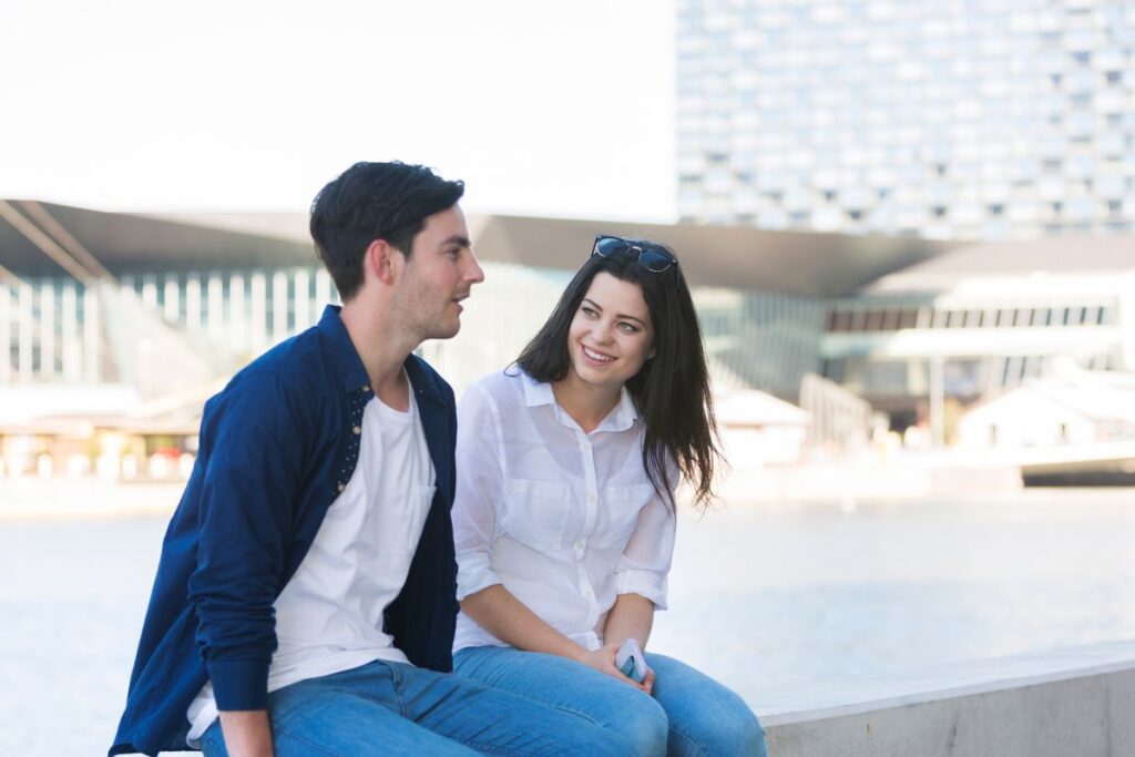 Dating couple sitting side by side, talking in a city landscape.