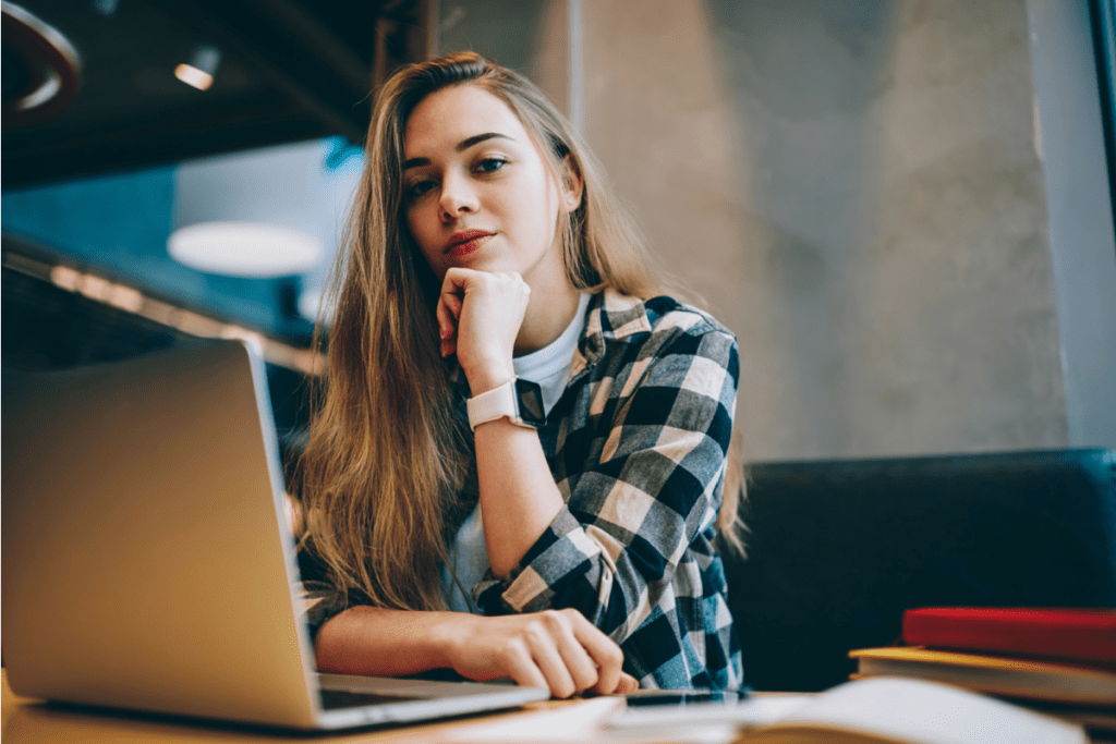 Young woman with long hair working on laptop in thoughtful posture.