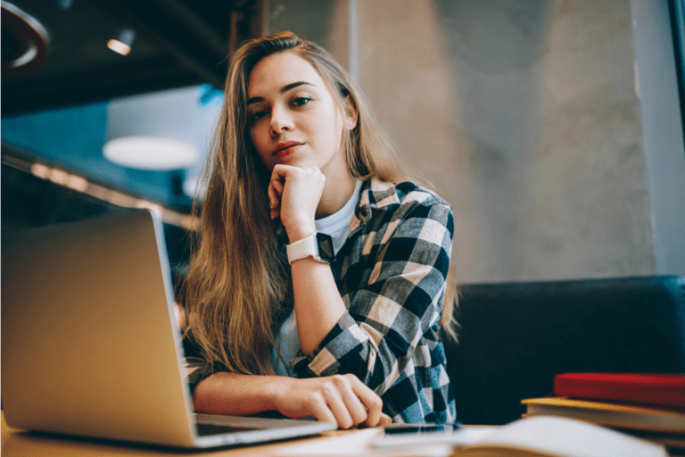 Woman with flannel shirt resting chin on her hand and working on laptop