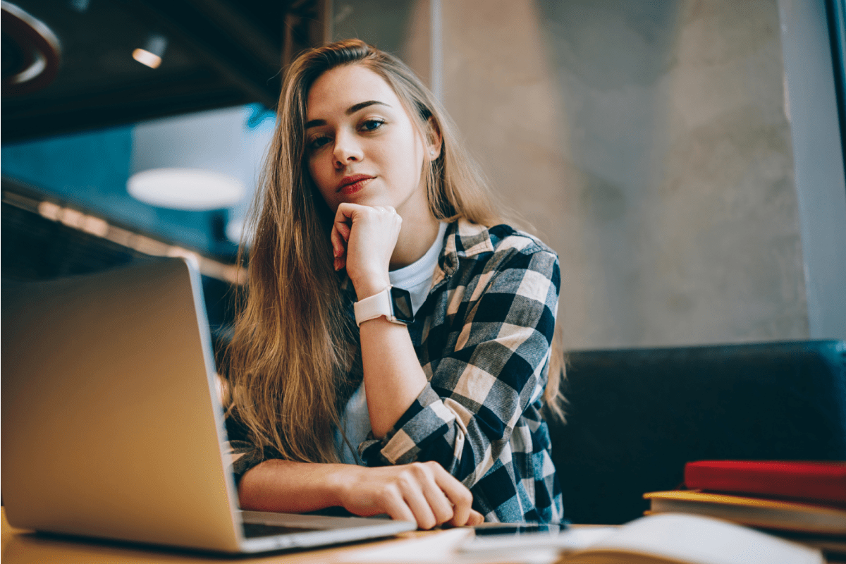 Woman with flannel shirt resting chin on her hand and working on laptop
