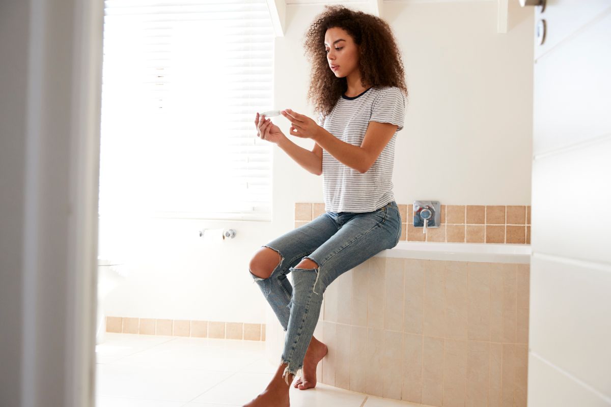 Woman sitting on side of bathtub holding pregnancy test