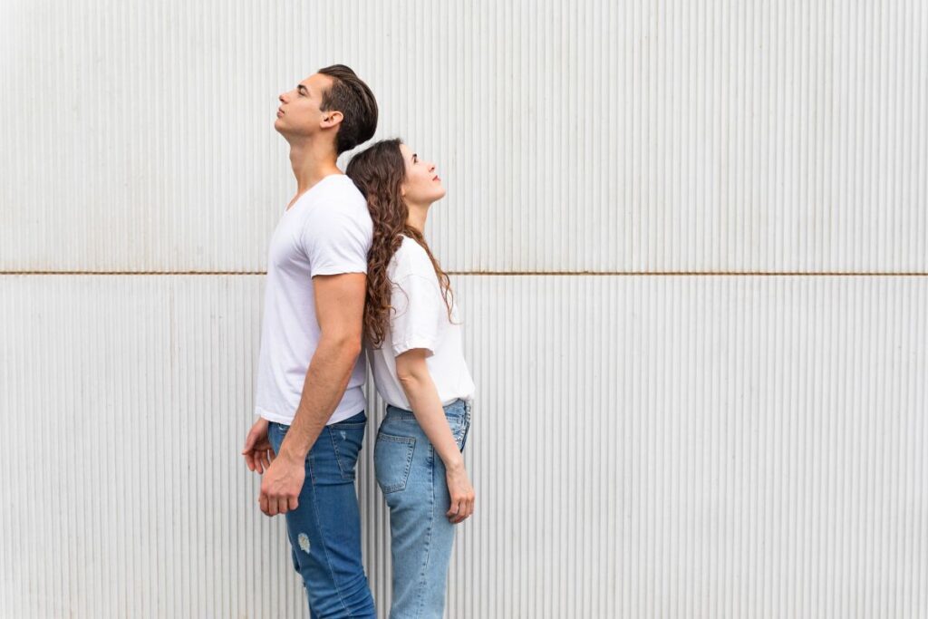 Young couple standing back to back, looking up, in front of a metal wall.