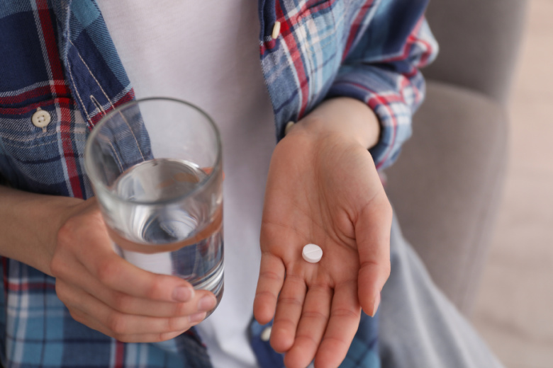 Woman holding pill in her hand with a glass of water, concept of taking abortion pill