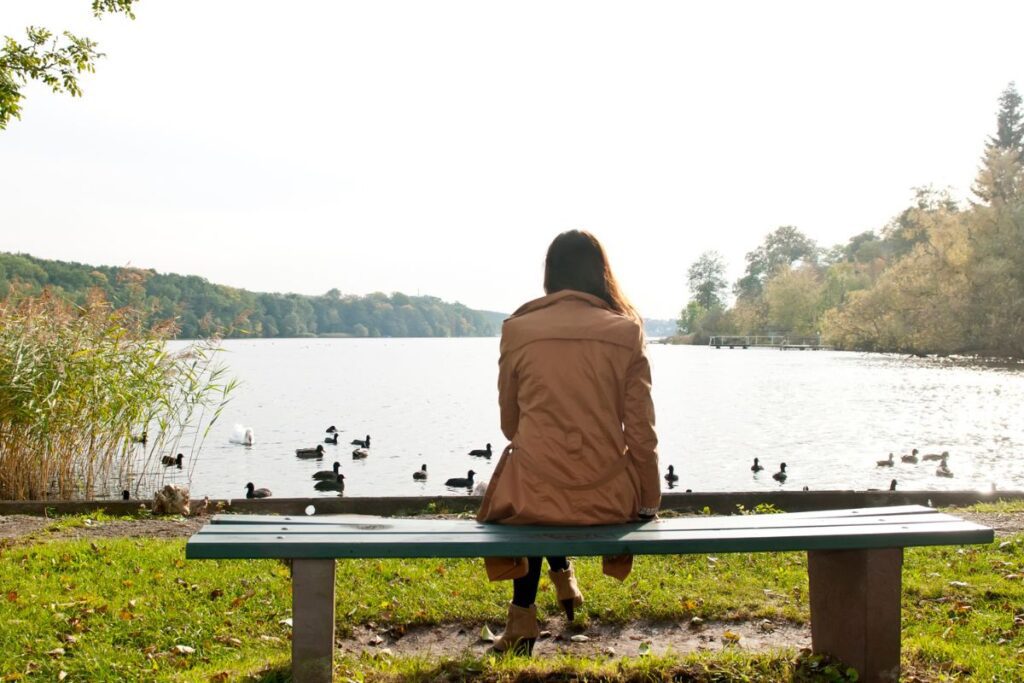 Woman sitting outside on a bench overlooking a lake, thinking.