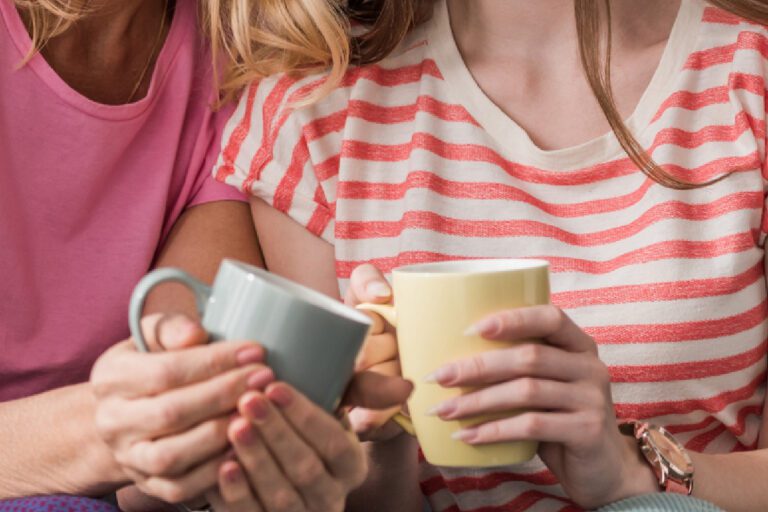 Two women holding coffee cups, chatting together.