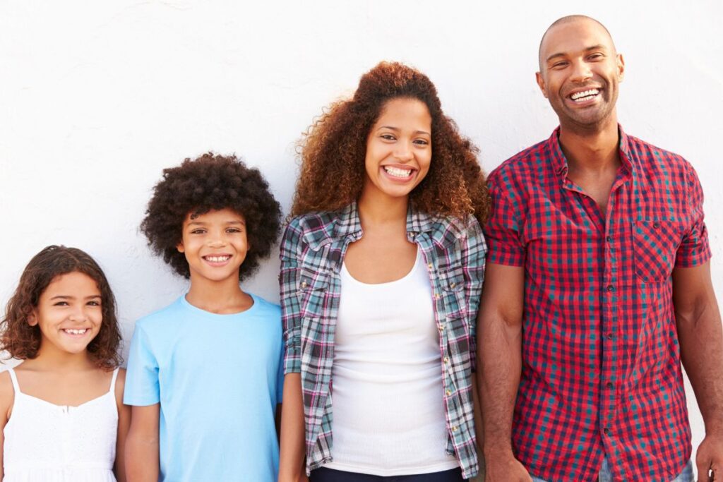 Happy African American family with two kids standing against a white wall.
