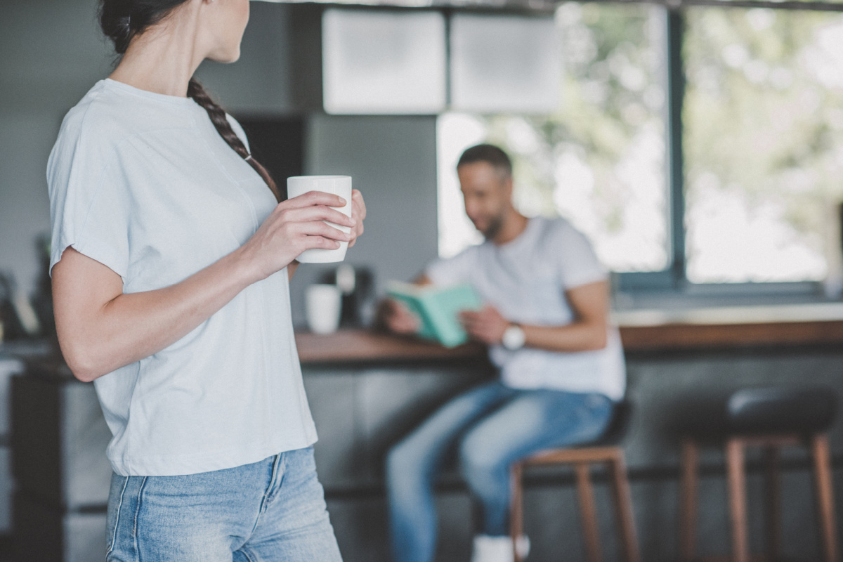 Woman standing in kitchen looking back at boyfriend sitting at counter.