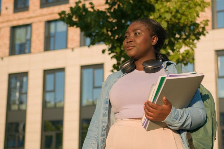 African American woman with headphones and notebooks on college campus.