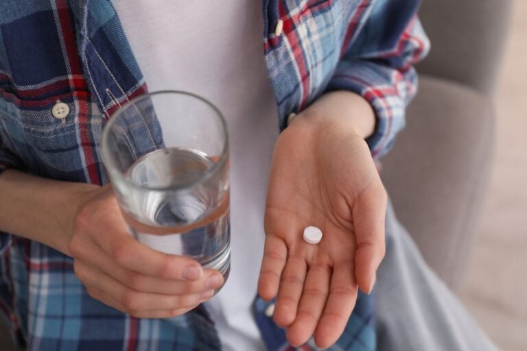 woman holding pill in hand with glass of water