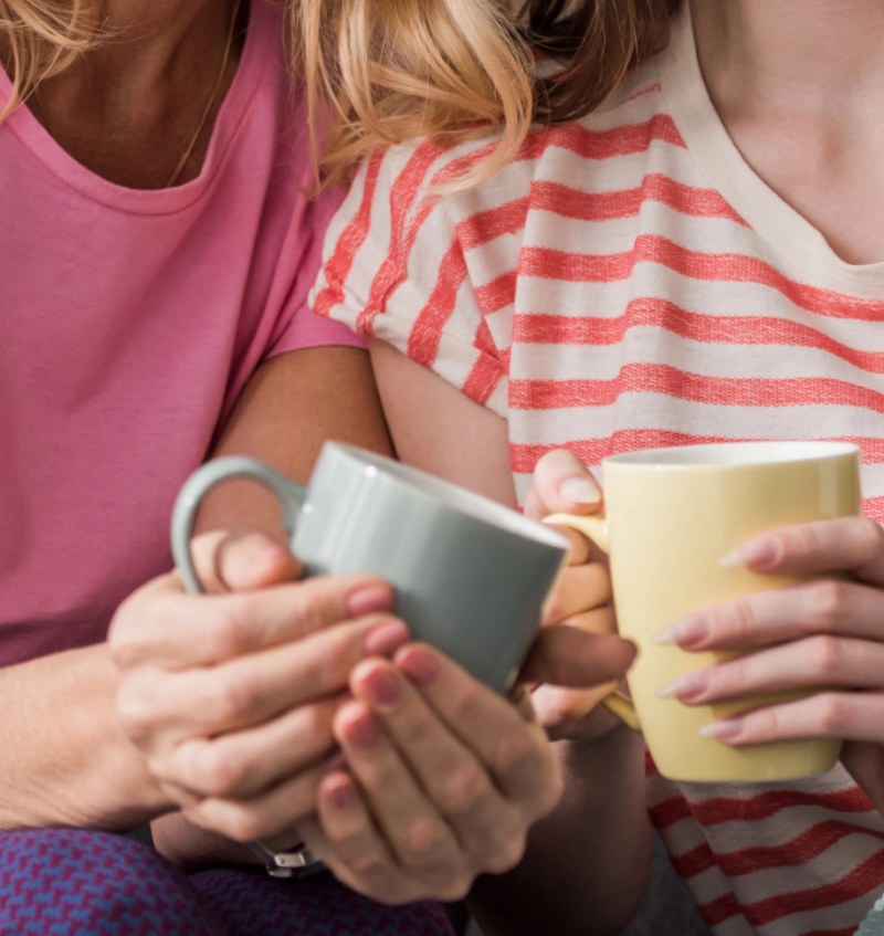 Two women holding coffee cups talking close together