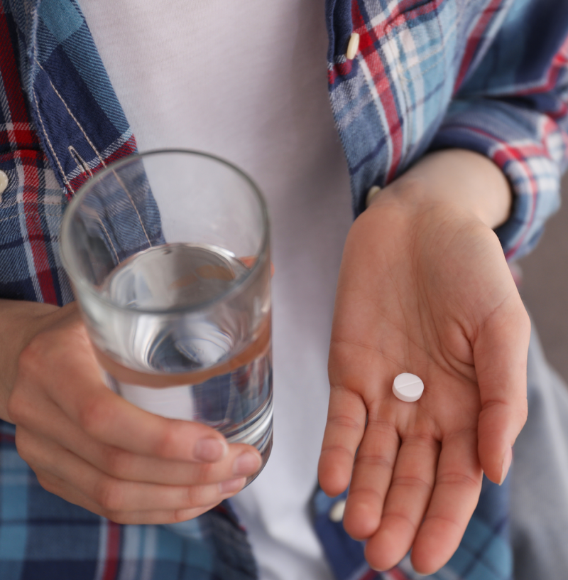 Woman in plaid shirt holding pill in her hand.