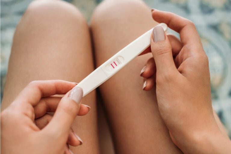 Woman holding a pregnancy test in her lap.
