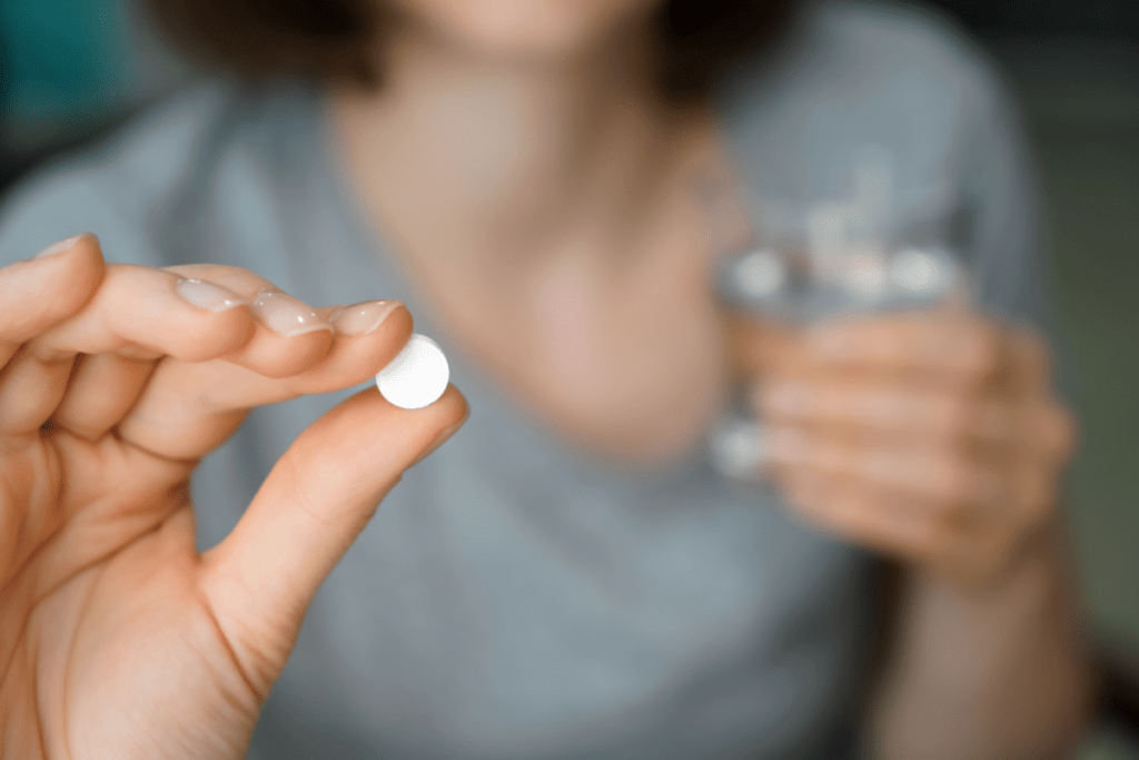 woman holding a pill in one hand and glass of water in another.